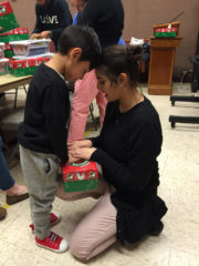 Annalisse, 17, prays over a shoebox with Seth, the 3-year-old son of Eric Huertas, Operation Christmas Child project leader for North Shore Spanish Baptist Church in Chicago, where Annalisse received Christ as Lord at a shoebox packing party three years ago.