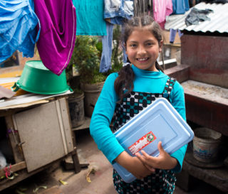 Paola proudly shows off her shoebox gift outside of her home.