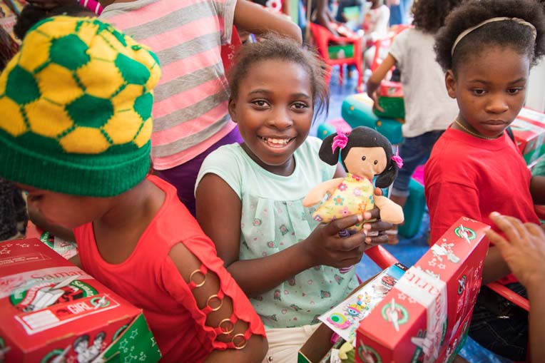 Girl smiling with doll at Operation Christmas Child shoebox event
