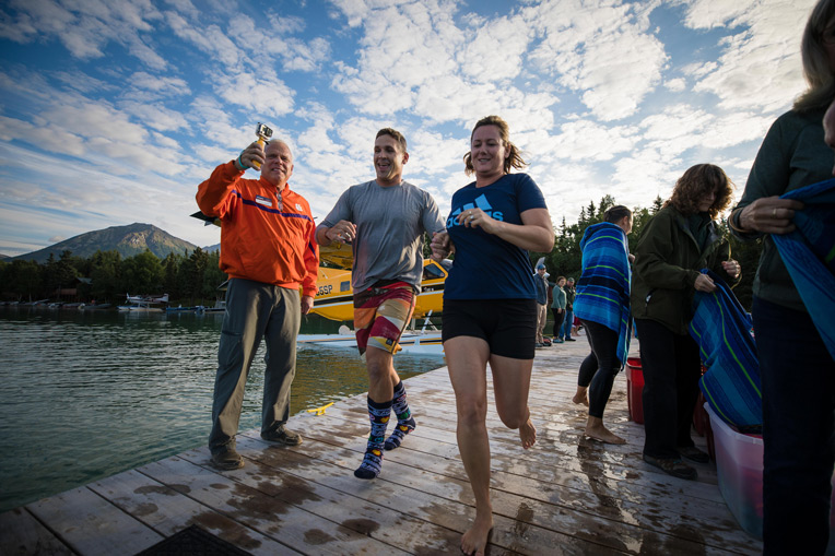 Marine Captain Schuyler Newsome run together toward the chilly waters of Lake Clark during the weekly polar plunge at Samaritan Lodge.