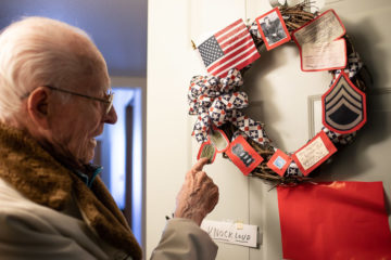 Theron points out a copy of his dog tags on the wreath commemorating his World War II service that hangs on his apartment door.