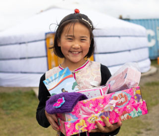 Una niña pequeña en Mongolia muestra los tesoros que recibió en su caja, incluyendo un librito de historias del Evangelio en su propio idioma.