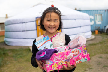 Una niña pequeña en Mongolia muestra los tesoros que recibió en su caja, incluyendo un librito de historias del Evangelio en su propio idioma.