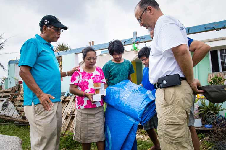 1893CQ-D-505: Pastor Manuelito Rey, left, of Cornerstone Community Church in Saipan prays for Chielo, Marion, and Mitch as they recieve tarps and solar lights from Samaritan's Purse.