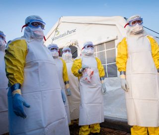 A group of medical workers in full body sanitation suites standing in front of a Samaritan's Purse medical tent.