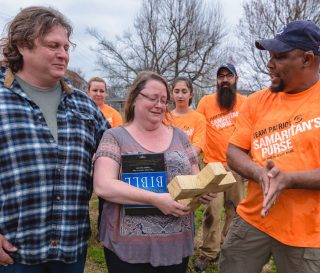 Marine Sergeant Robert Bogus presents a Bible and also a chainsaw-cut cross to homeowners Christy and Travis Autry.