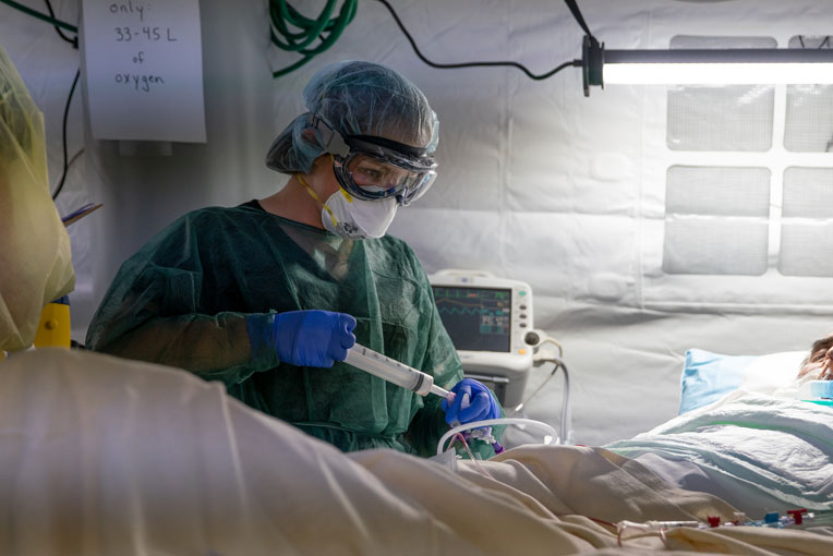 A nurse checks a patient's feeding tube in the ICU.
