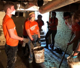 Volunteers work hard in a flooded basement removing mud and silt from a broken dam and an overflowing river.