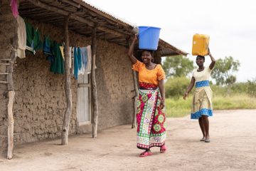 Eunice and her daughter carry water back to their home. 