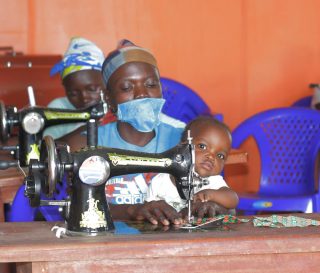 A mother learns to sew at our safe place in Bunia while her young child looks on.