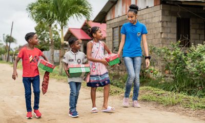 Teen leads children with shoebox gifts.
