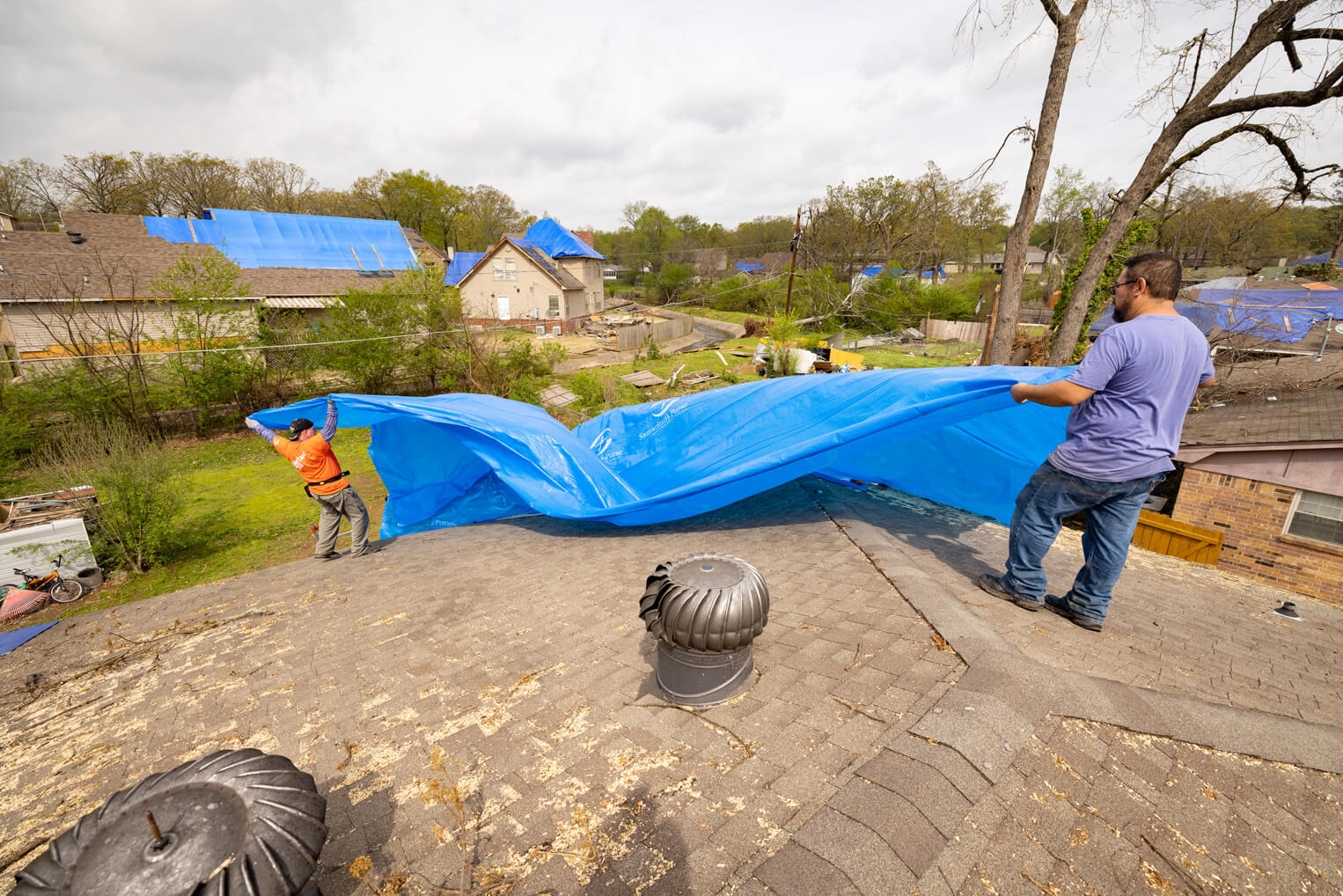 Homeowner Rey Tobias helps volunteer Ken Perry place tarp on the roof ahead of yet another storm.