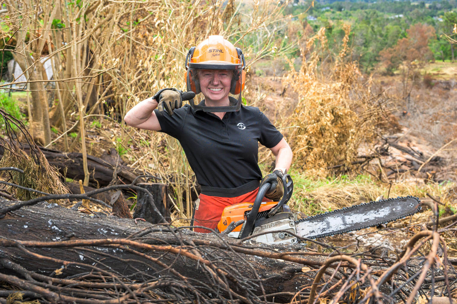 A volunteer operates a chainsaw to cut up a fire-damaged tree in Maui.