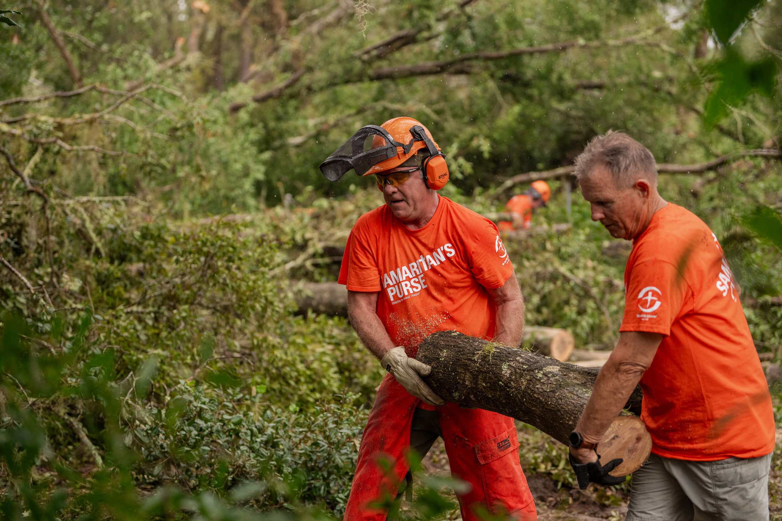 Two Samaritan's Purse volunteers carry a large log to a pile on the edge of the property.