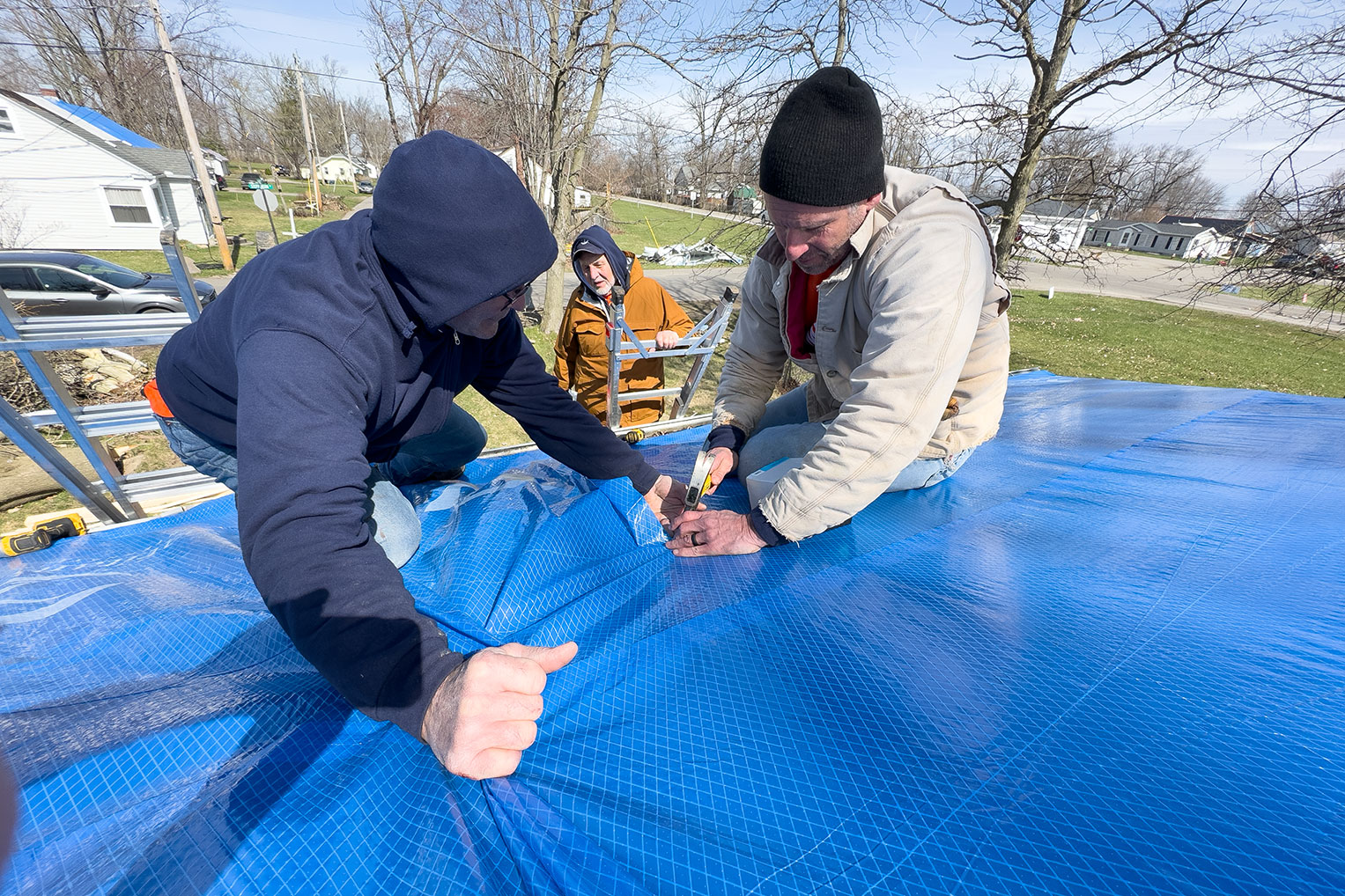 Volunteers tarp a damaged roof to protect the home from the elements and further damage.