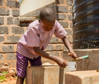 A student in Kenya tests the water system, preparing to enjoy a drink of clean water.