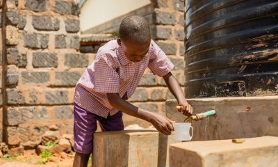 Un estudiante en Kenia prueba el sistema de agua, y se prepara para disfrutar un vaso con agua potable.