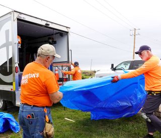 Samaritan's Purse volunteers, wearing our signature orange shirts, unload our blue Samaritan's Purse tarp from our truck in the Midwest.