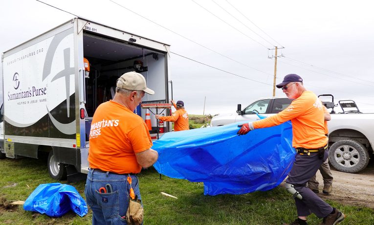 Samaritan's Purse volunteers, wearing our signature orange shirts, unload our blue Samaritan's Purse tarp from our truck in the Midwest.