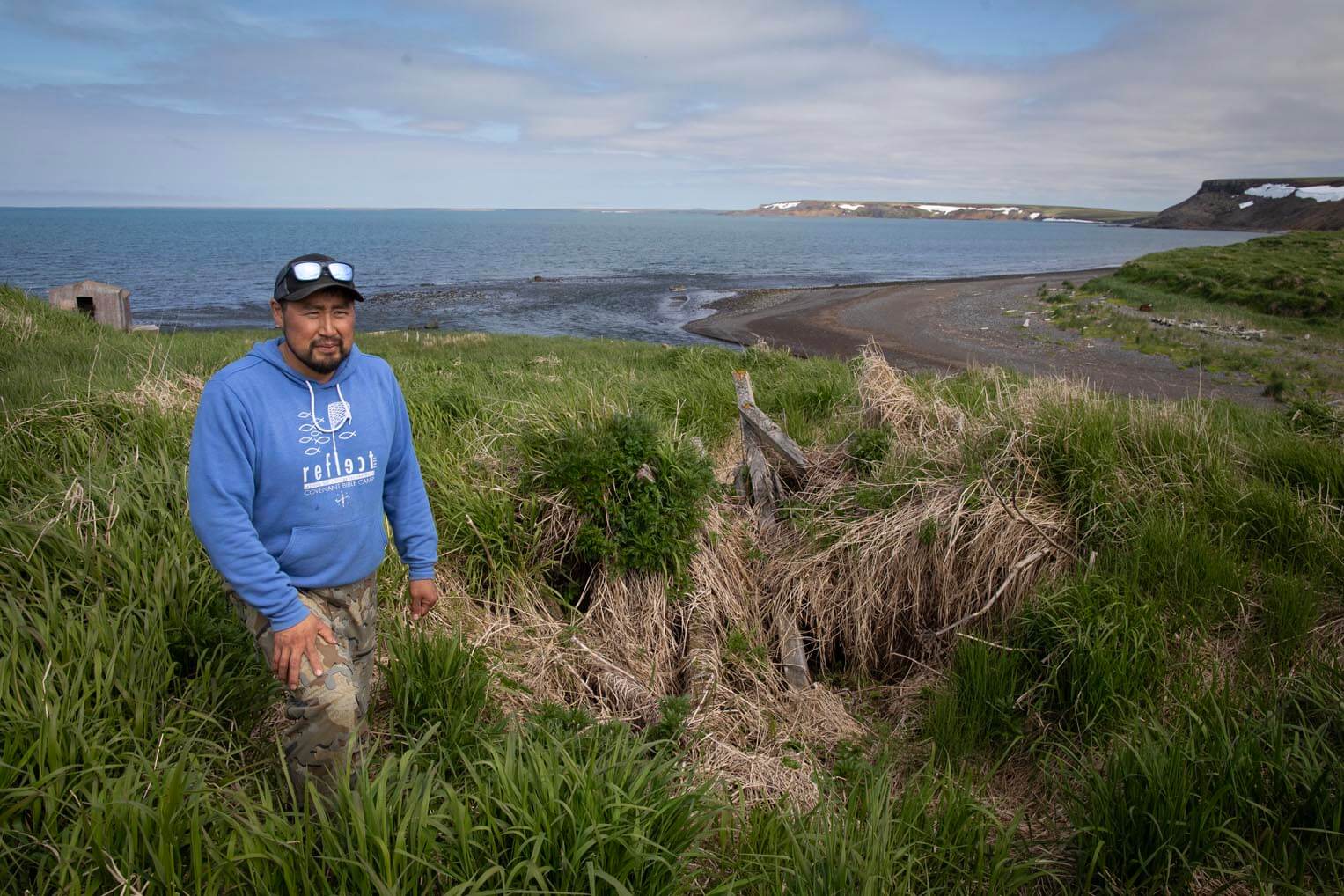 Ed Kiokun stands in the high grass at the site of his grandparents' semi-subterranean dugout at Nash Harbor.