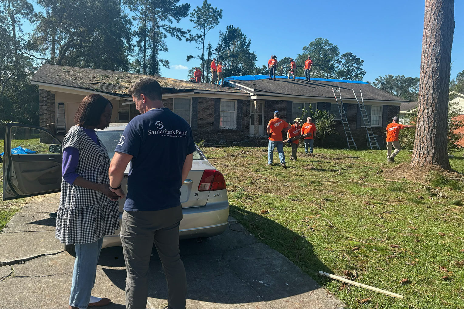 Samaritan's Purse staff member prays with Mariah while volunteers work on her damaged home.