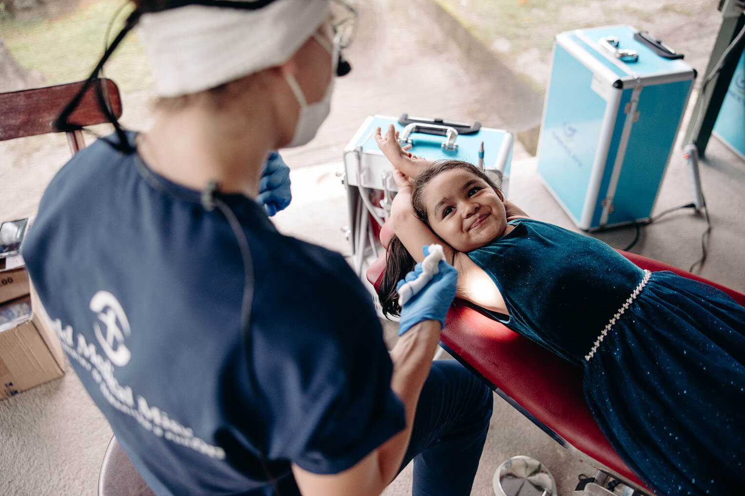 Between patients, Marya, the team's dental hygienist, allows a curious young girl to try the dental chair and teaches her how to brush her teeth.