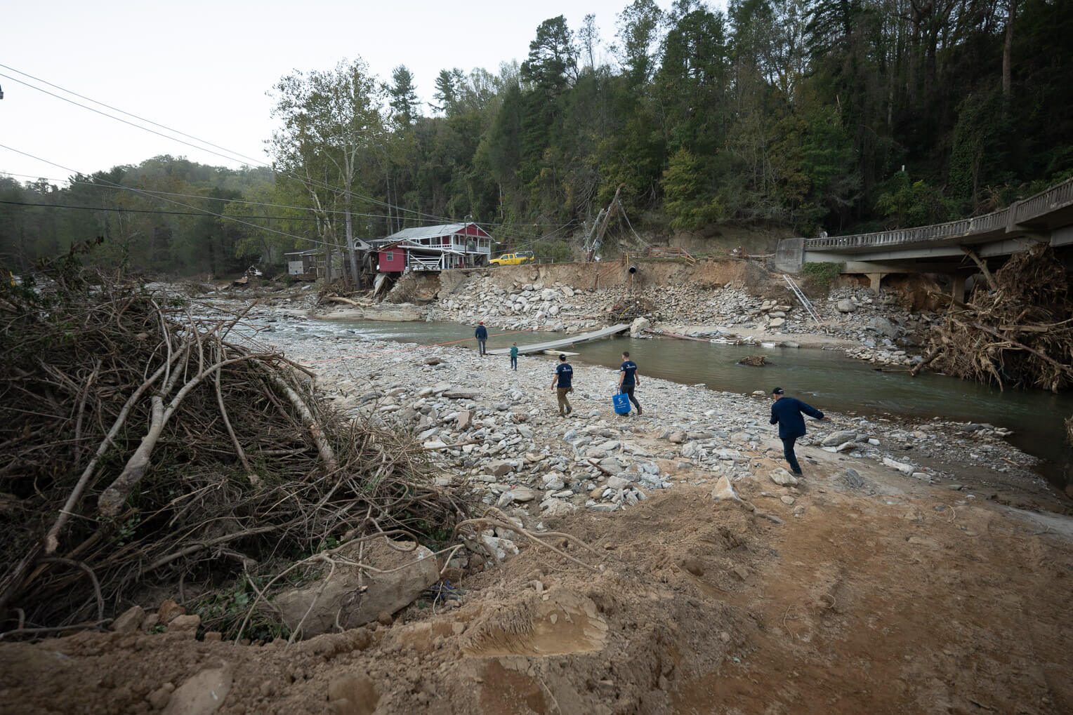 Samaritan's Purse DART members carry a Starlink unit across a footbridge on the Broad River in Bat Cave, North Carolina. The unit was donated to the Bat Cave Volunteer Fire Department, which was largely cut off from road access when a bridge washed out during Hurricane Helene flooding.