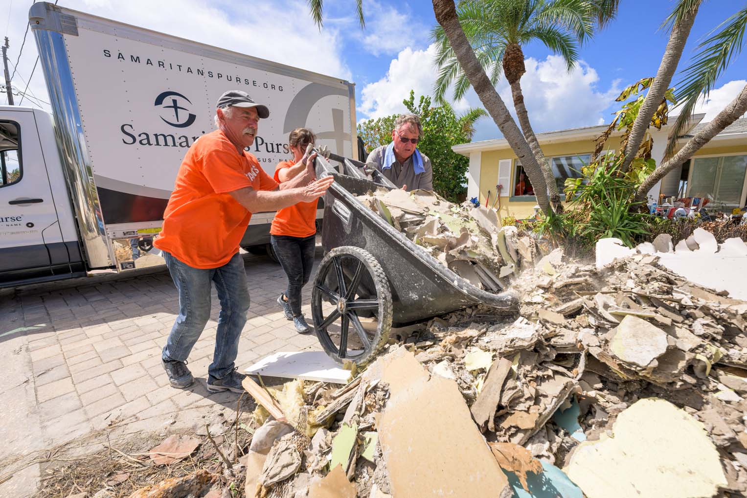 Volunteers wheel out debris onto streets lined with the insides of flooded homes.