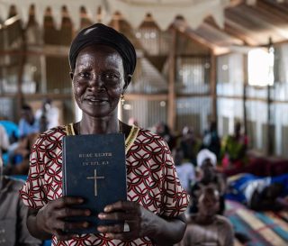 Elizabeth tiene en sus manos la Palabra de Dios, la cual ahora puede leer y enseñar, después de que aprendió a leer en idioma nuer, gracias a nuestro programa eclesiástico de alfabetización.