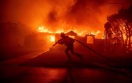 A firefighter battles the Palisades Fire as it burns a structure in the Pacific Palisades neighborhood of Los Angeles, Tuesday, Jan. 7, 2025. (AP Photo/Ethan Swope)