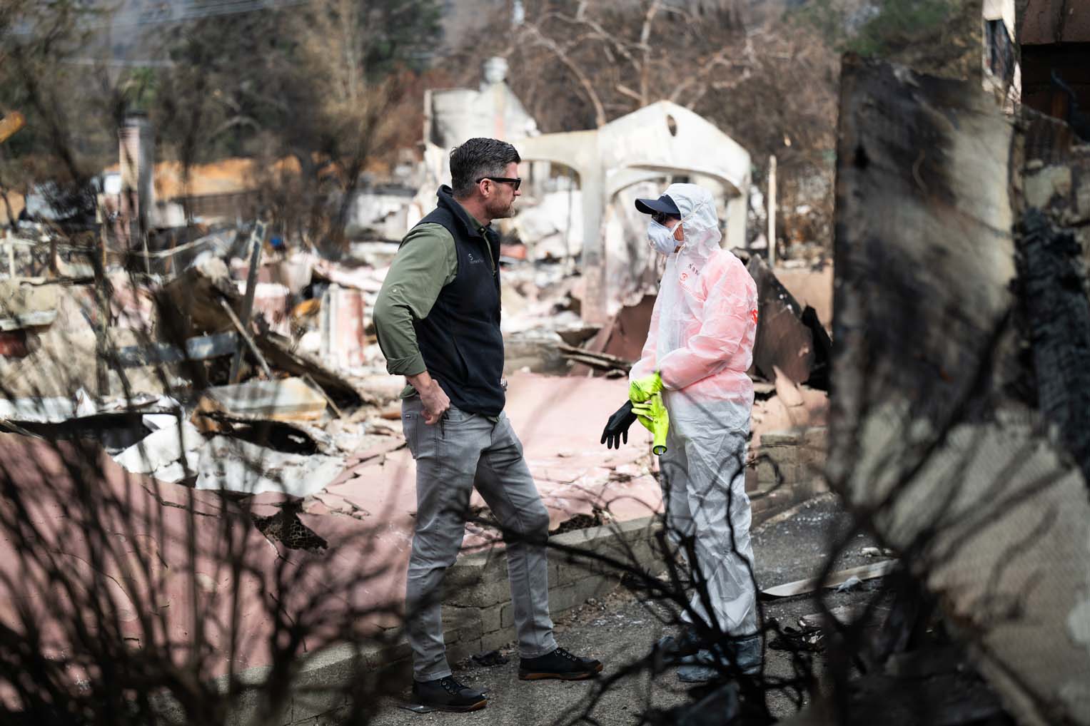 Edward Graham meets with a volunteer amid the rubble of a wildfire-destroyed home.