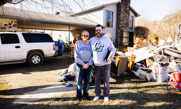 Brandt Justice (right) and his father Gary Justice stand in the Justices' yard where flood water came through, filling their home. Our volunteers helped clean out damaged belongings, walls, and flooring.