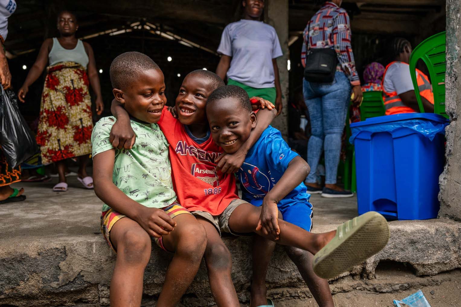 Three friends laugh on the church steps while their parents wait for care inside. In a place marked by hardship, childhood joy remains resilient.