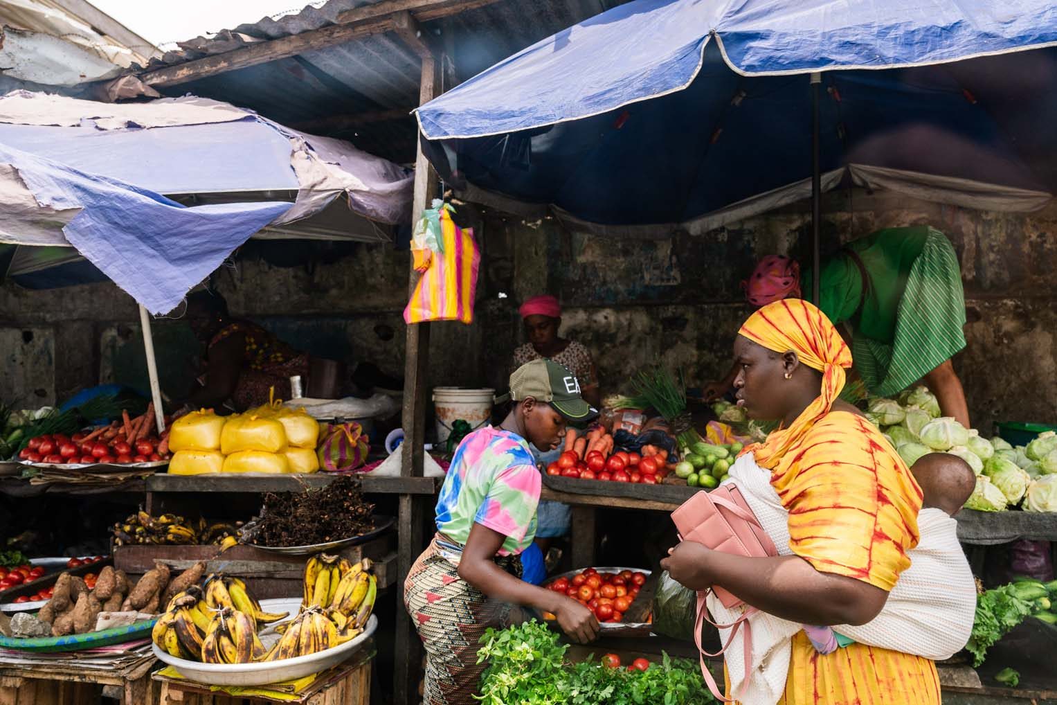 A mother shops for vegetables at an open-air stall.
