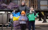 Mother and two children load bicycle with seed potatoes and watering can