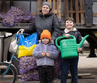 Mother and two children load bicycle with seed potatoes and watering can