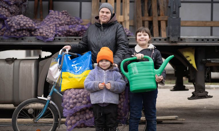 Mother and two children load bicycle with seed potatoes and watering can