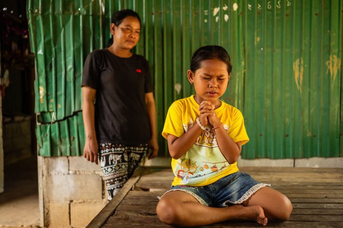 Cambodian girl prays for her mother as she looks on