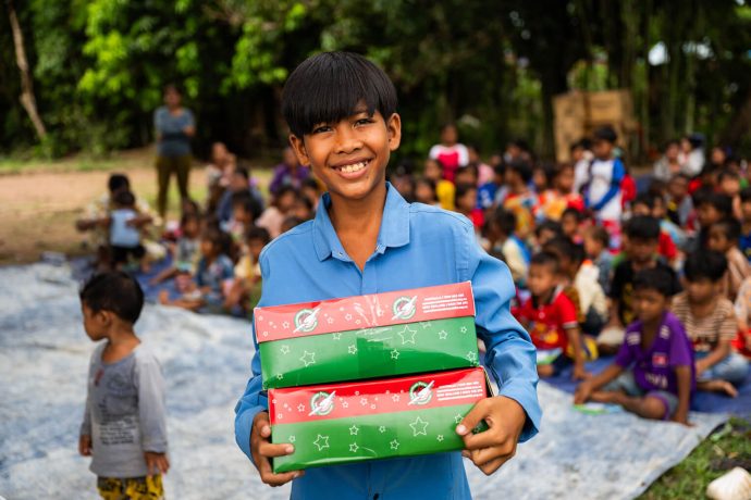 Cambodian boy hands out shoeboxes to other children
