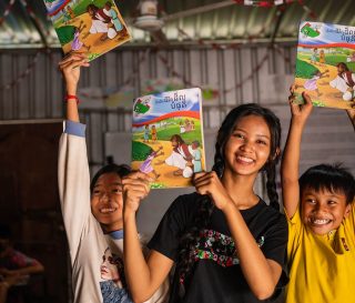 Samnang and two of her students joyfully hold up The Greatest Journey workbooks