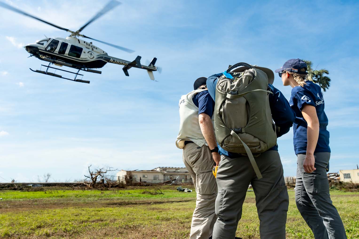Three Samaritan’s Purse disaster response workers watch a helicopter take off to deliver aid in Jamaica after Hurricane Melissa.