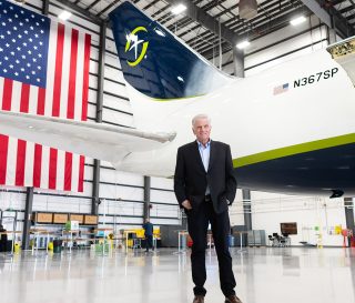 Samaritan's Purse President Franklin Graham stands inside a large aircraft hangar in front of a Samaritan’s Purse cargo plane, with a large American flag hanging behind the aircraft’s tail.