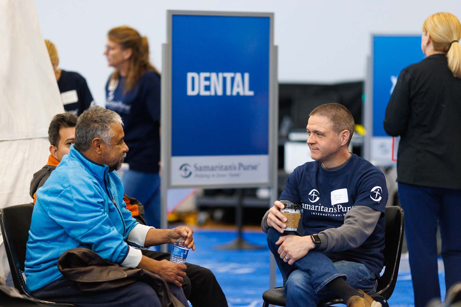 Un voluntario se sienta con un paciente para animarlo mientras espera un examen médico.