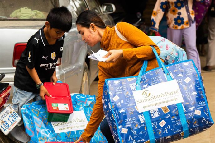 A mother and son leave a Samaritan's Purse distribution site with tarp, a bag full of other essential supplies, and an Operation Christmas Child gift-filled shoebox.