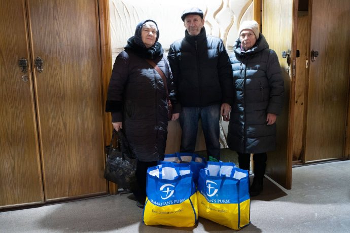 Oksana, Andrii, and neighbor with bags of food from Samaritan's Purse