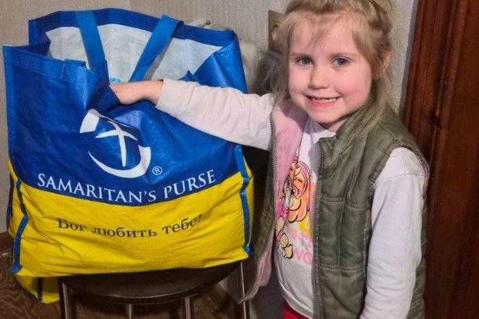 Yana's smiling daughter with Samaritan's Purse branded bag of groceries