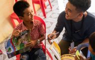 Sann interacts with a student of The Greatest Journey over his workbook