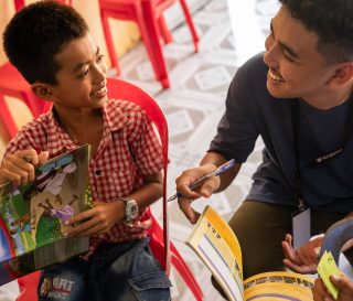Sann interacts with a student of The Greatest Journey over his workbook