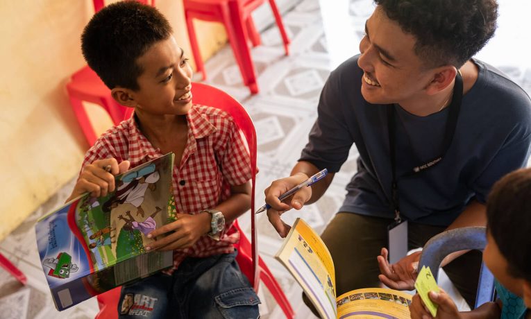 Sann interacts with a student of The Greatest Journey over his workbook