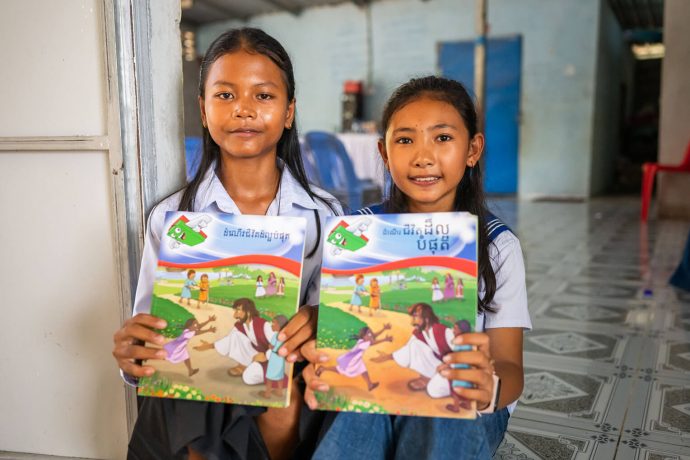 Chea and Dara hold up their student workbooks